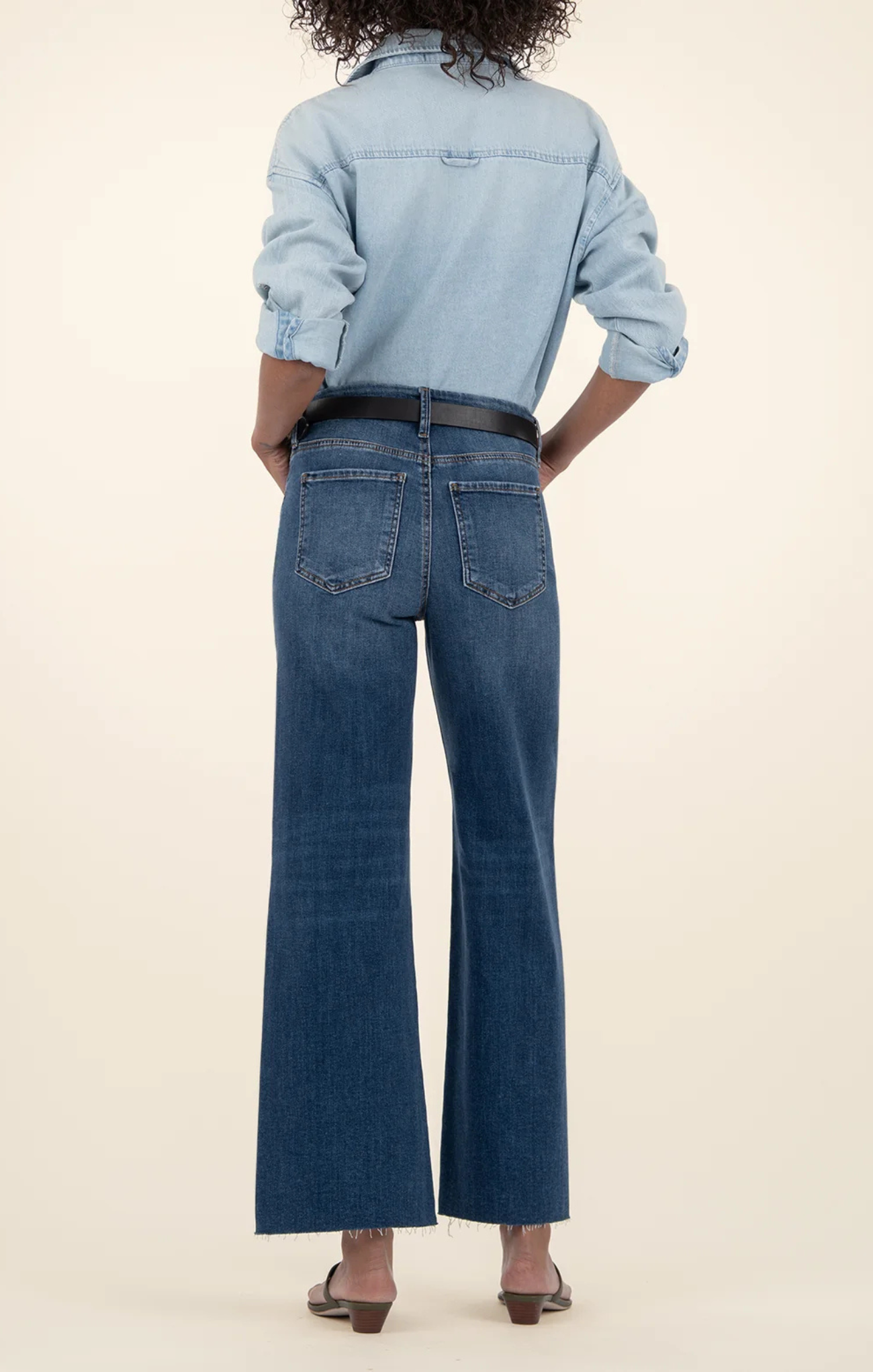 Person wearing a light blue denim shirt and dark blue jeans on a beige background