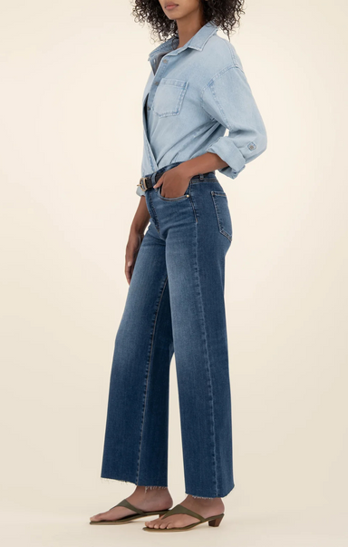 Person wearing a light blue denim jacket and dark blue jeans on a beige background