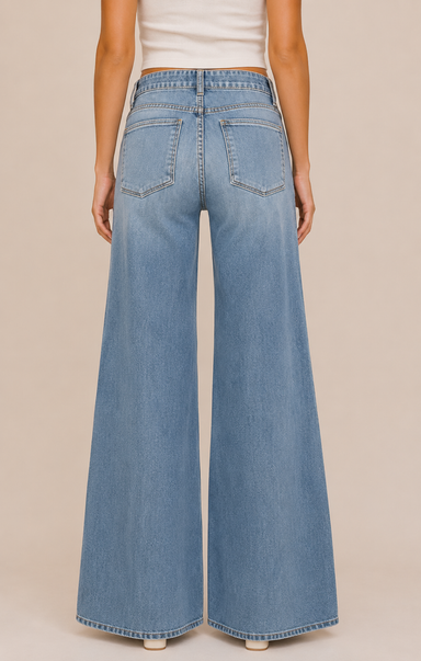 A person shown from the back wearing light-wash blue wide-leg denim jeans and a white ribbed top, standing against a plain beige studio background.