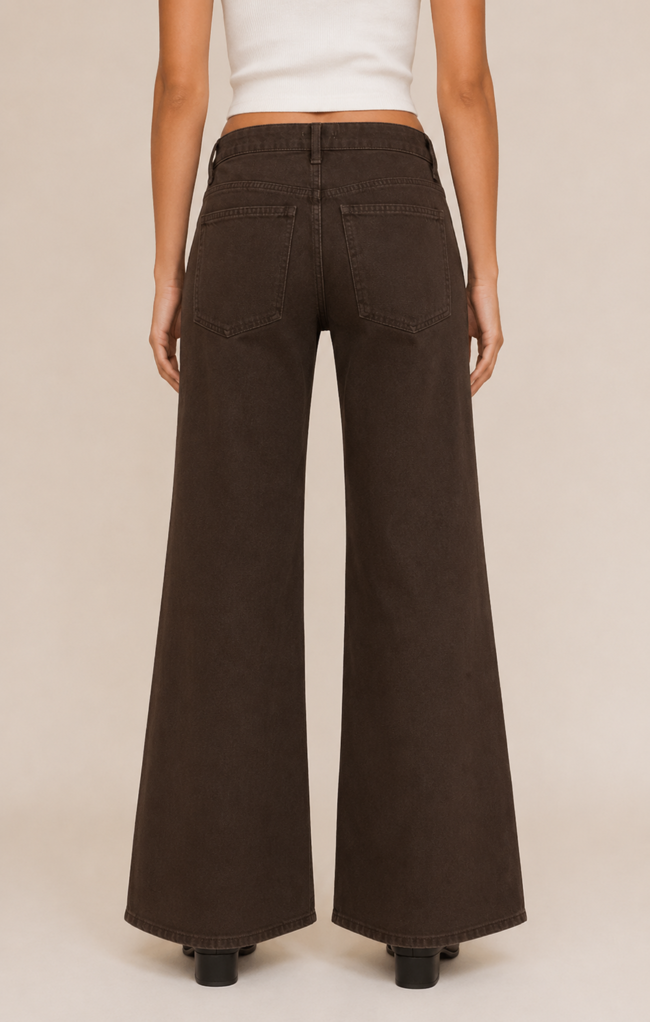 A model shown from the back wearing dark brown wide-leg jeans and a white cropped top, standing against a solid light beige background.
