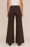 A model shown from the back wearing dark brown wide-leg jeans and a white cropped top, standing against a solid light beige background.