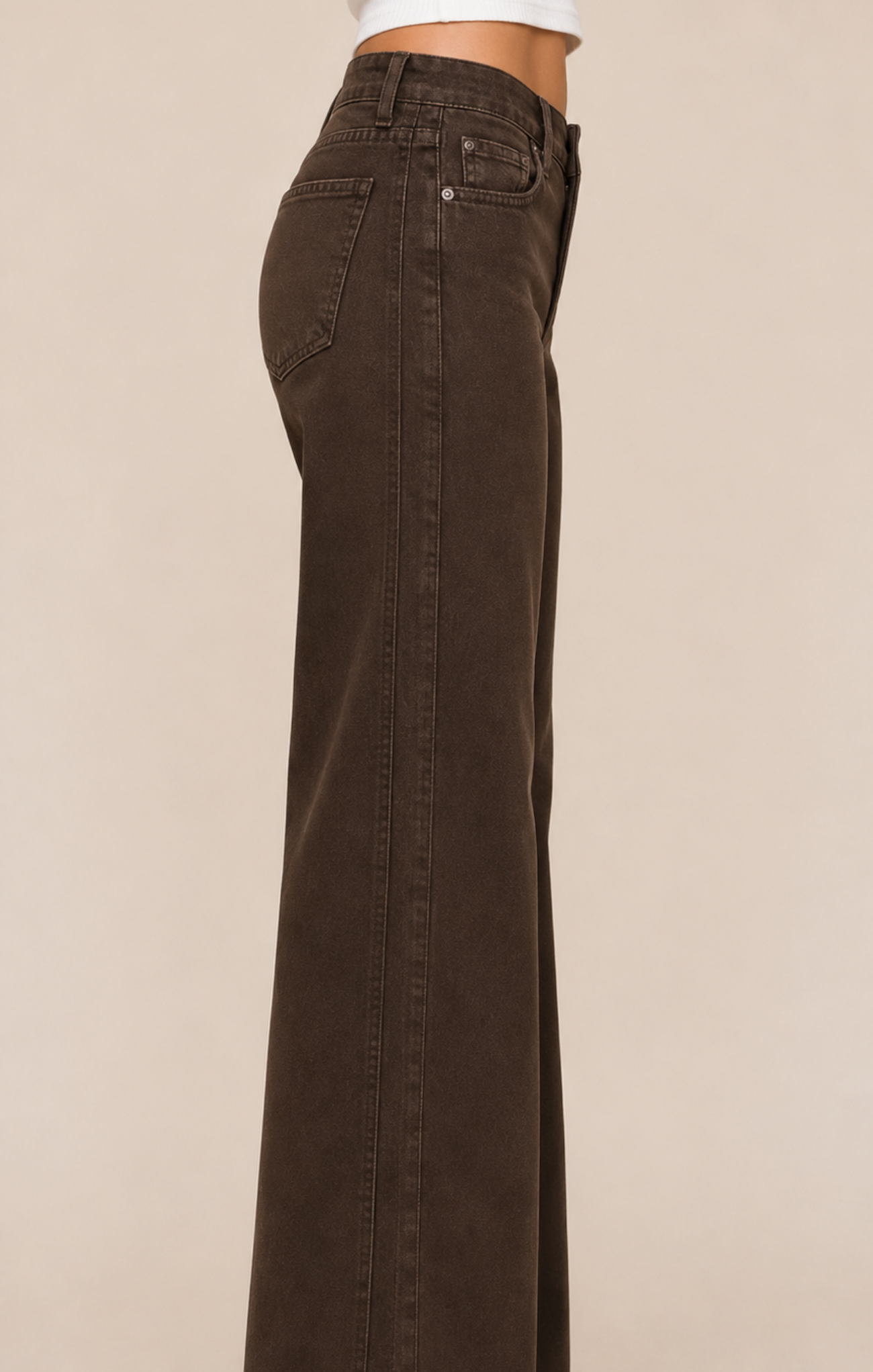 A side profile view of a person wearing dark brown wide-leg jeans against a solid beige background.