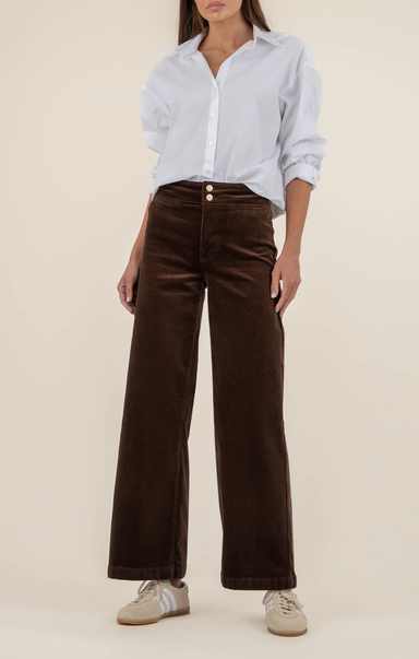 Person wearing a light blue button-up shirt and brown wide-leg pants on a beige background