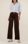 Person wearing a light blue button-up shirt and brown wide-leg pants on a beige background