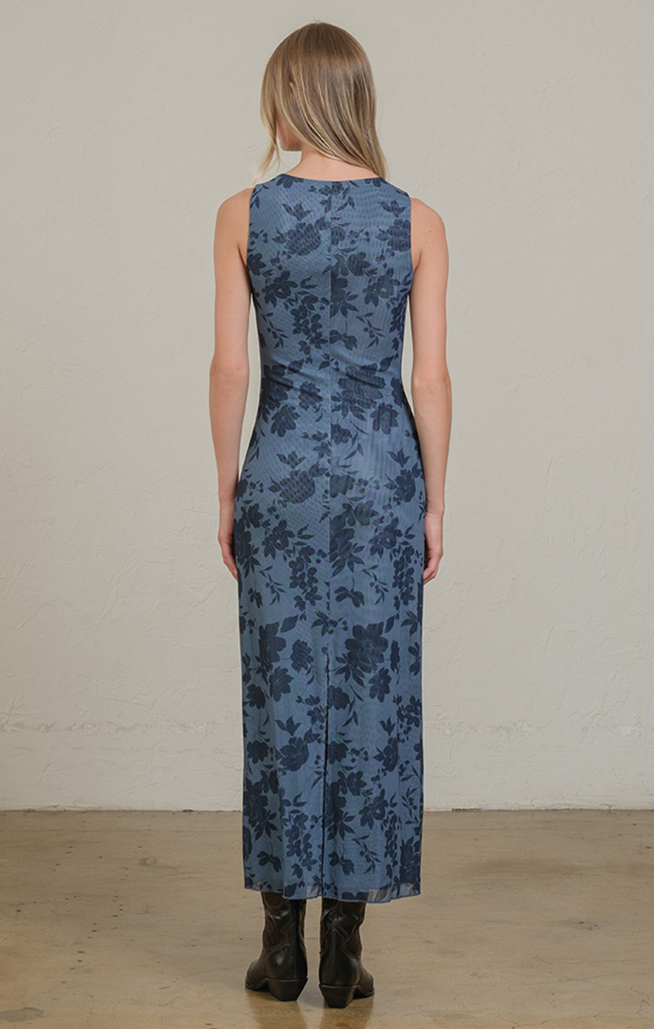 Woman wearing a sleeveless blue floral dress against a plain background