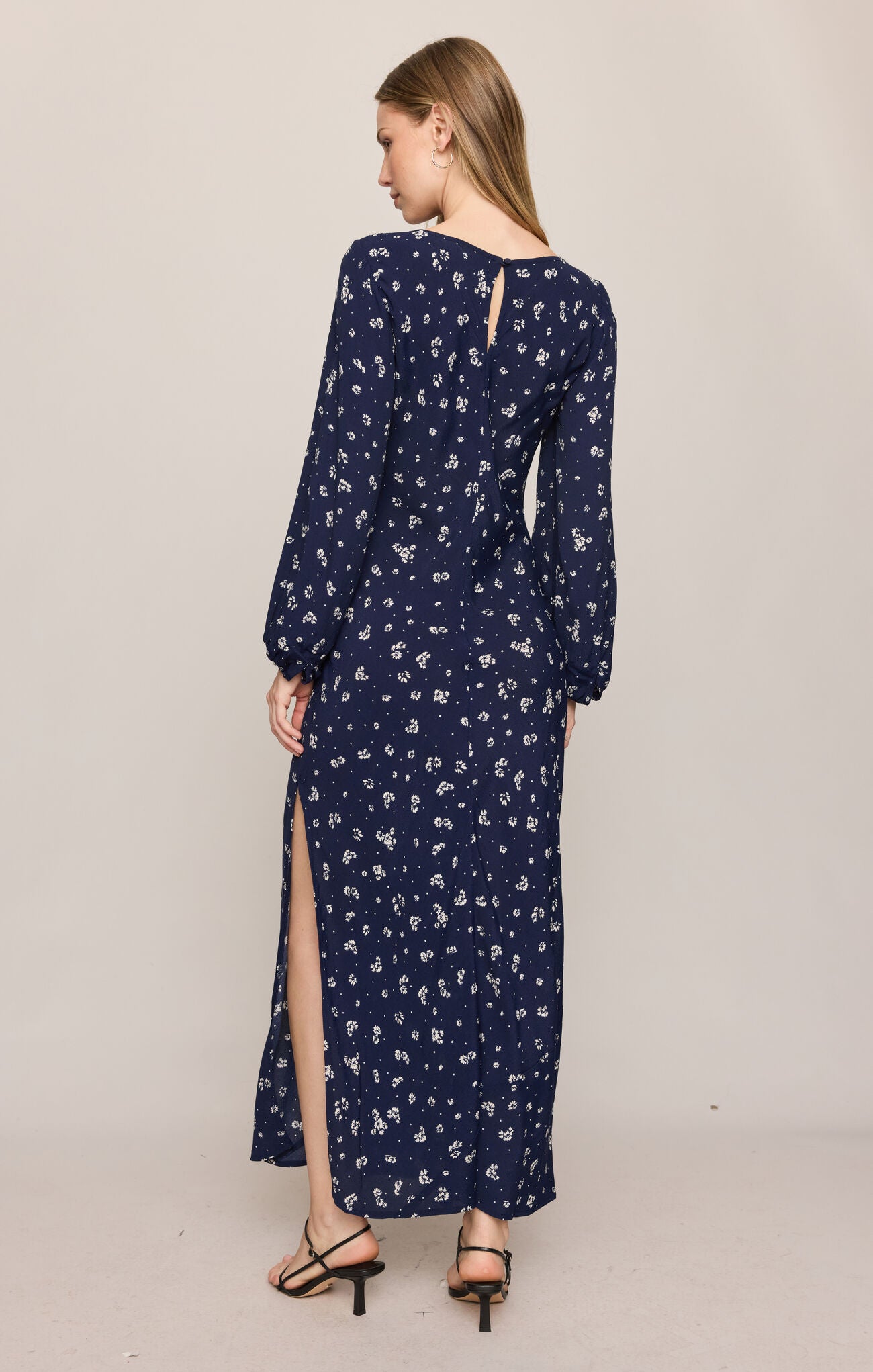 Woman wearing a navy blue floral dress with long sleeves and a slit on a beige background