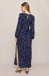 Woman wearing a navy blue floral dress with long sleeves and a slit on a beige background
