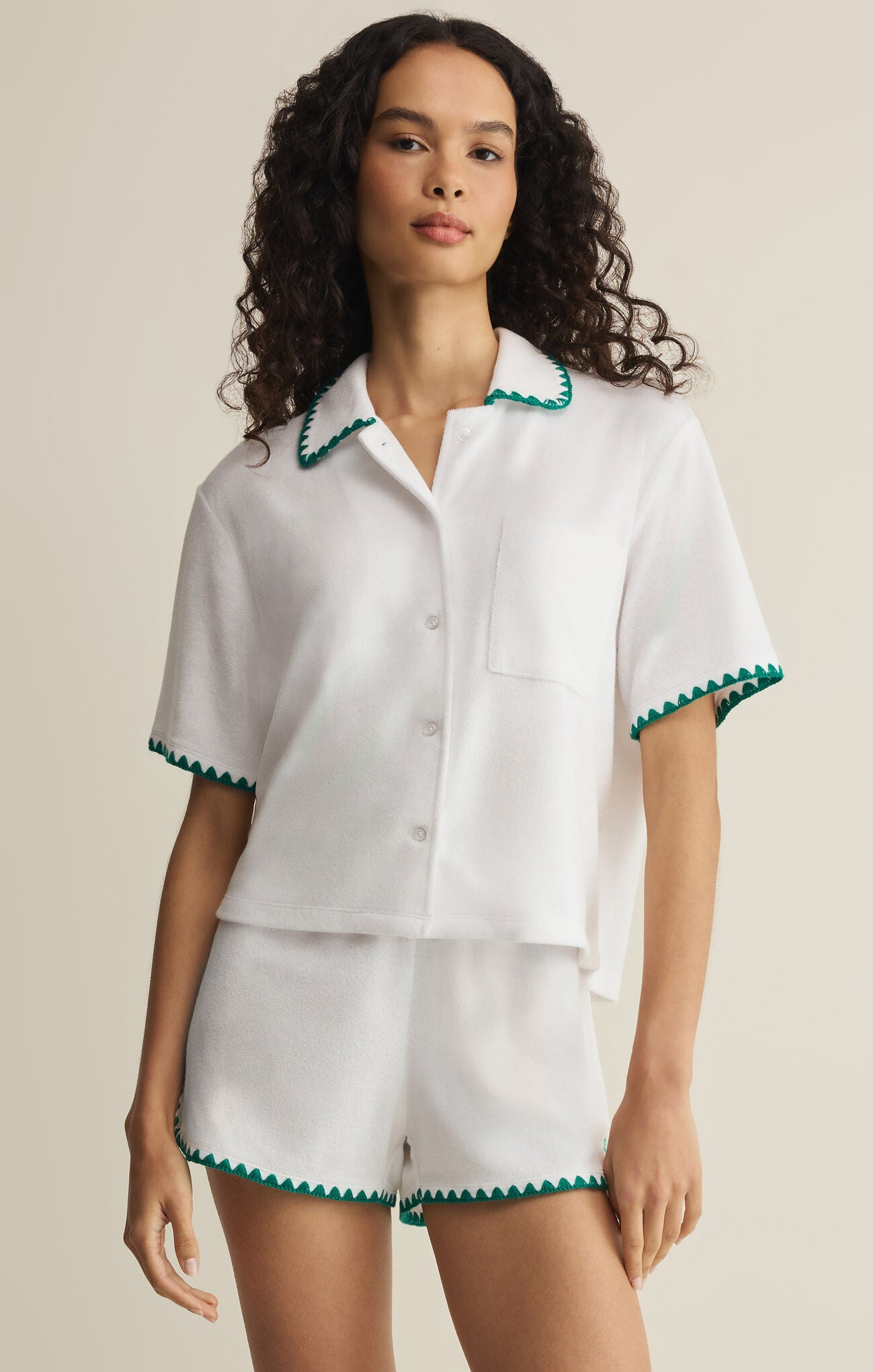 Woman wearing a white outfit with green trim on a beige background