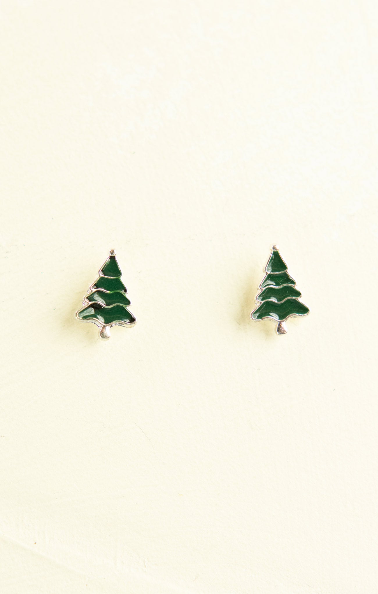 Green tree-shaped earrings on a beige background