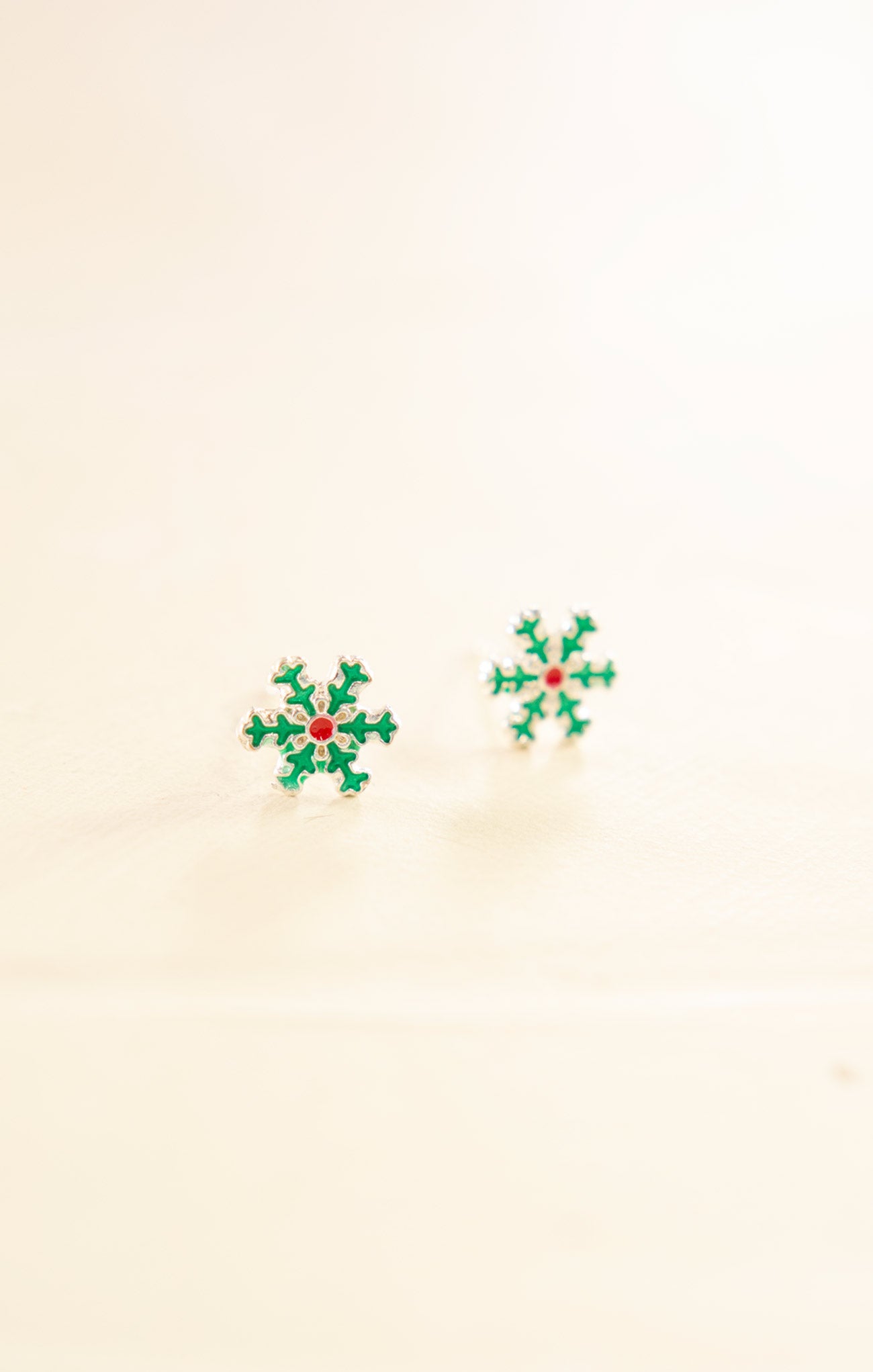 Pair of green snowflake earrings on a beige background