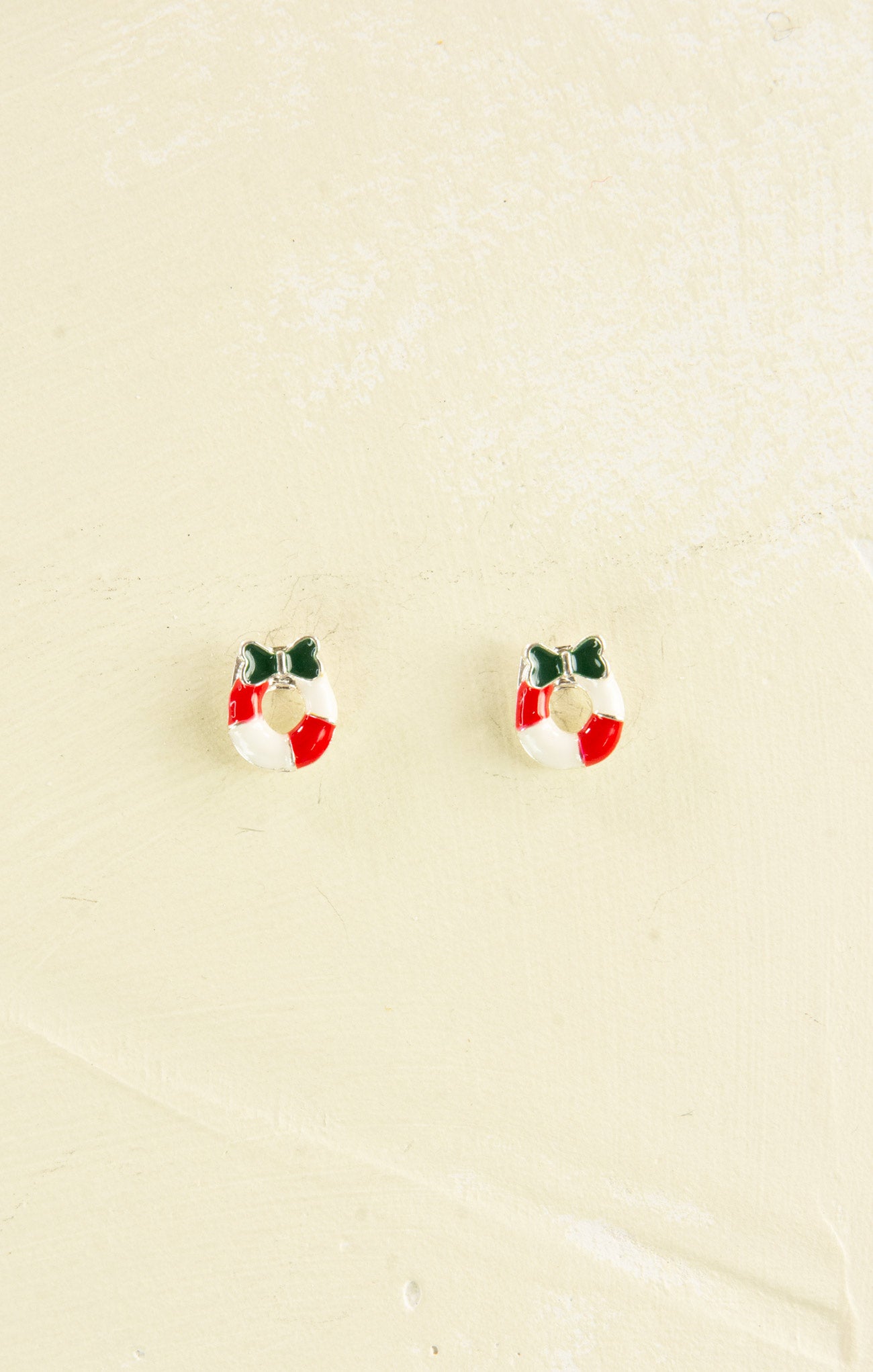 Small earrings shaped like Christmas wreaths on a beige background