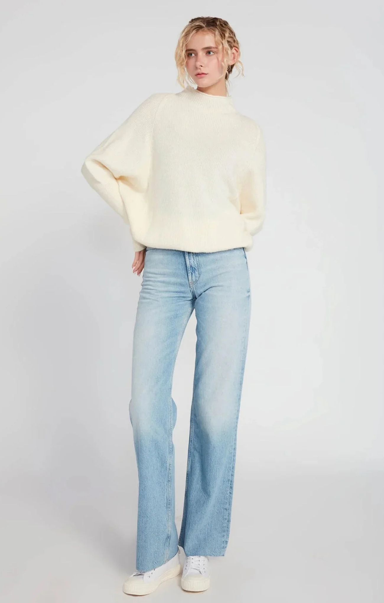 Person wearing a cream sweater and light blue jeans on a white background
