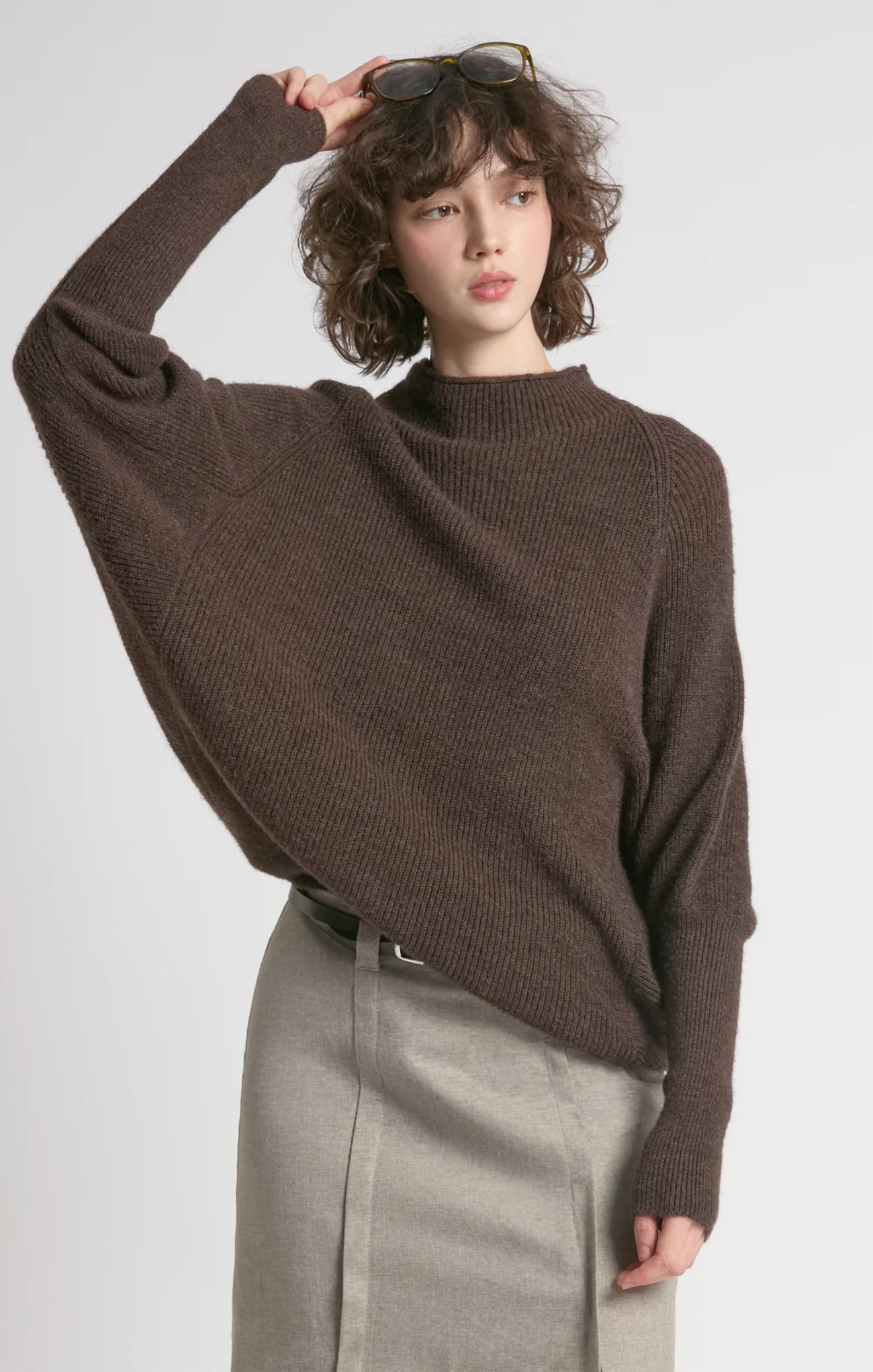 Person wearing a brown sweater and gray pants against a white background