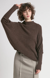 Person wearing a brown sweater and gray pants against a white background