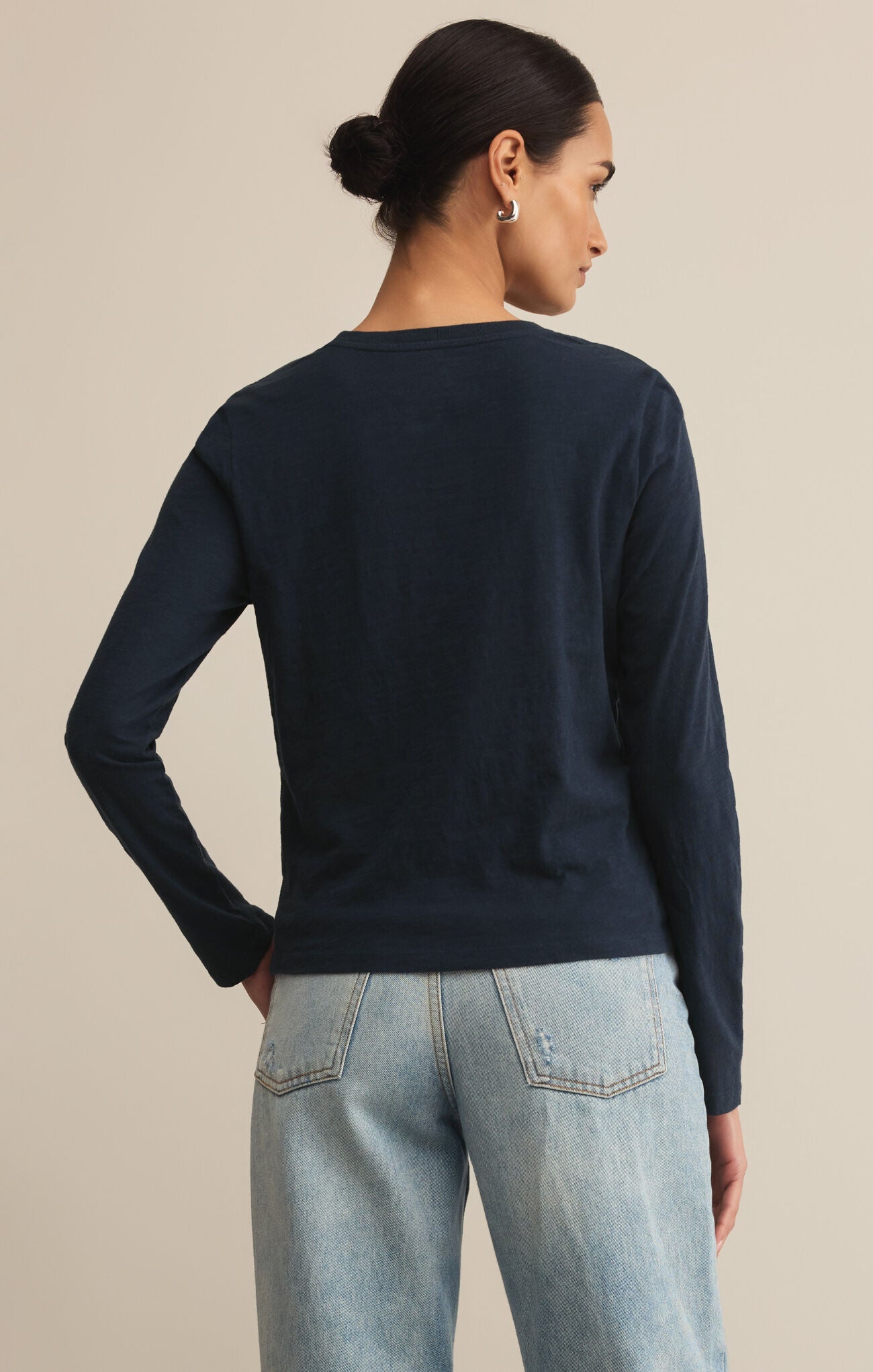 Person wearing a navy sweater and light blue jeans on a beige background