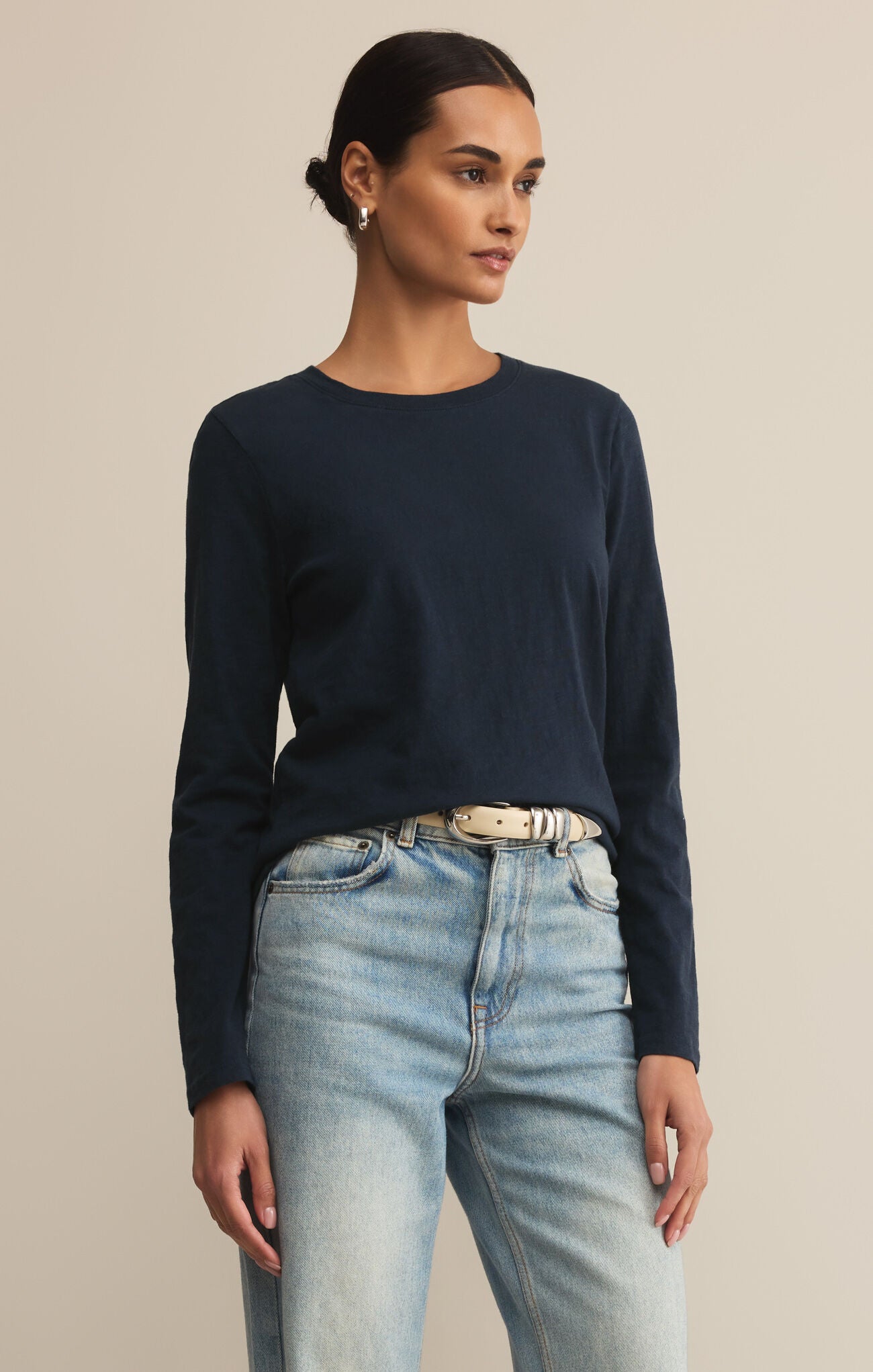 Woman wearing a navy long-sleeve top and light blue jeans against a beige background