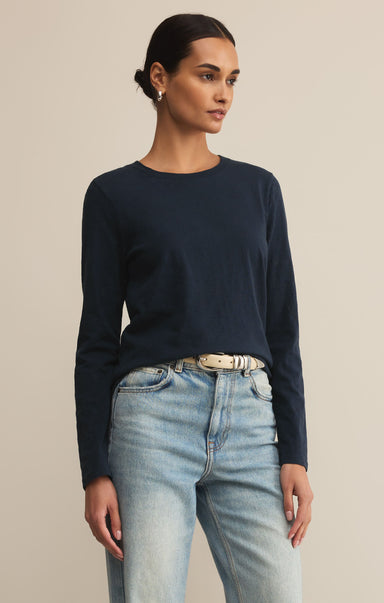 Woman wearing a navy long-sleeve top and light blue jeans against a beige background