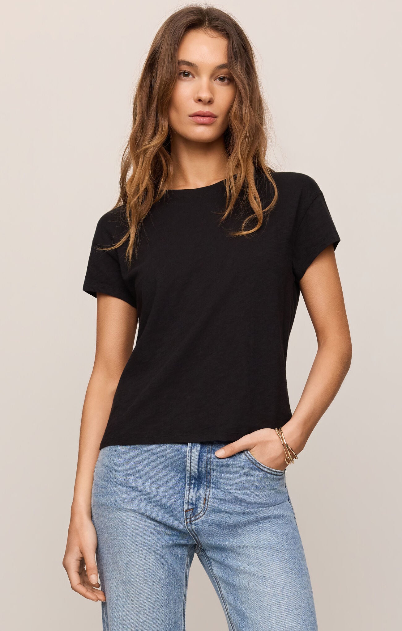 Woman wearing a black t-shirt and blue jeans against a plain background