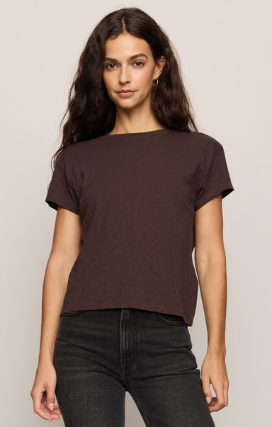 Woman wearing a brown t-shirt and black pants against a plain background