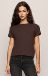 Woman wearing a brown t-shirt and black pants against a plain background