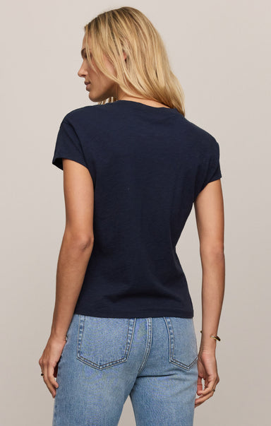 Woman wearing a navy blue t-shirt and light blue jeans on a plain background