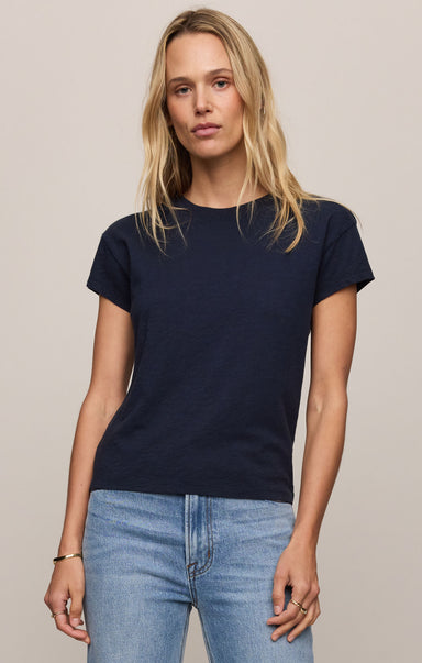 Woman wearing a navy blue t-shirt and light blue jeans against a beige background