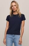 Woman wearing a navy blue t-shirt and light blue jeans against a beige background