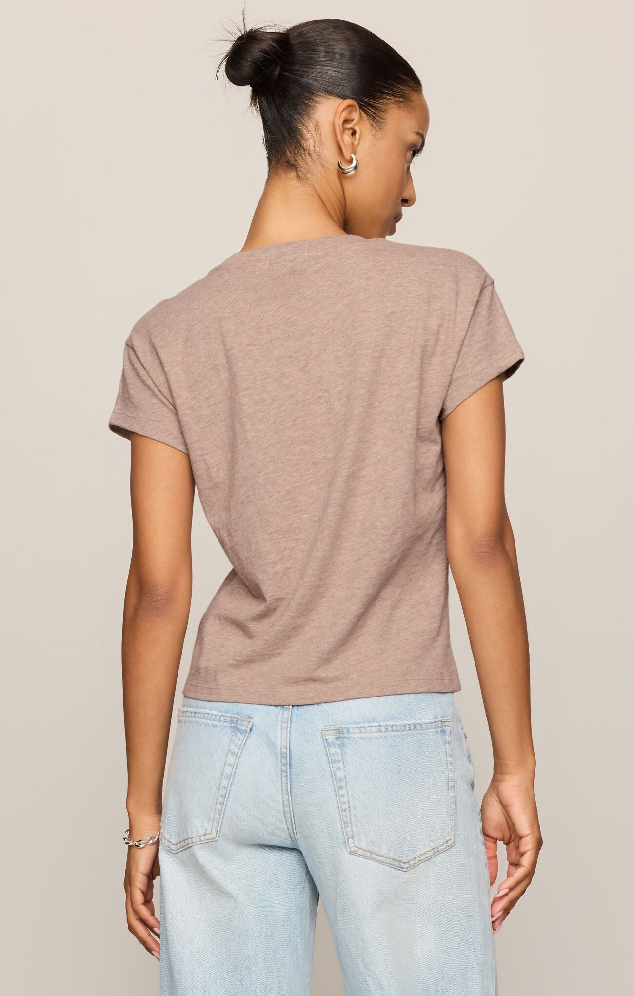 Woman wearing a brown t-shirt and light blue jeans against a beige background