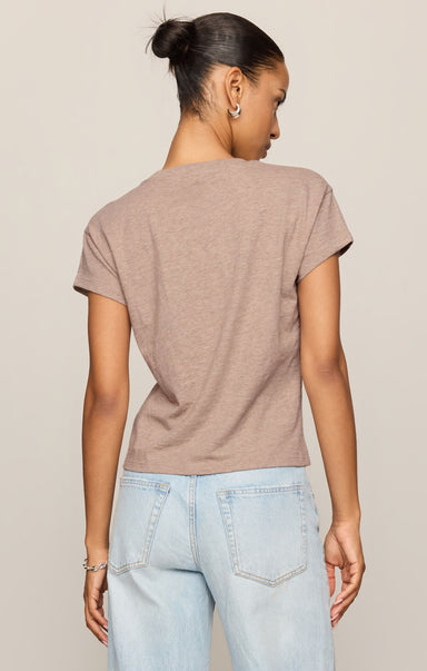 Woman wearing a brown t-shirt and light blue jeans against a beige background