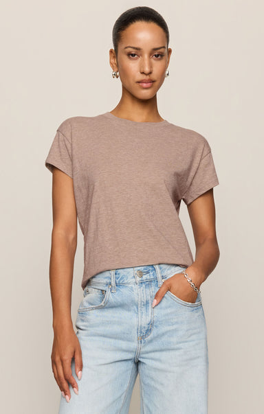 Woman wearing a brown t-shirt and light blue jeans against a beige background