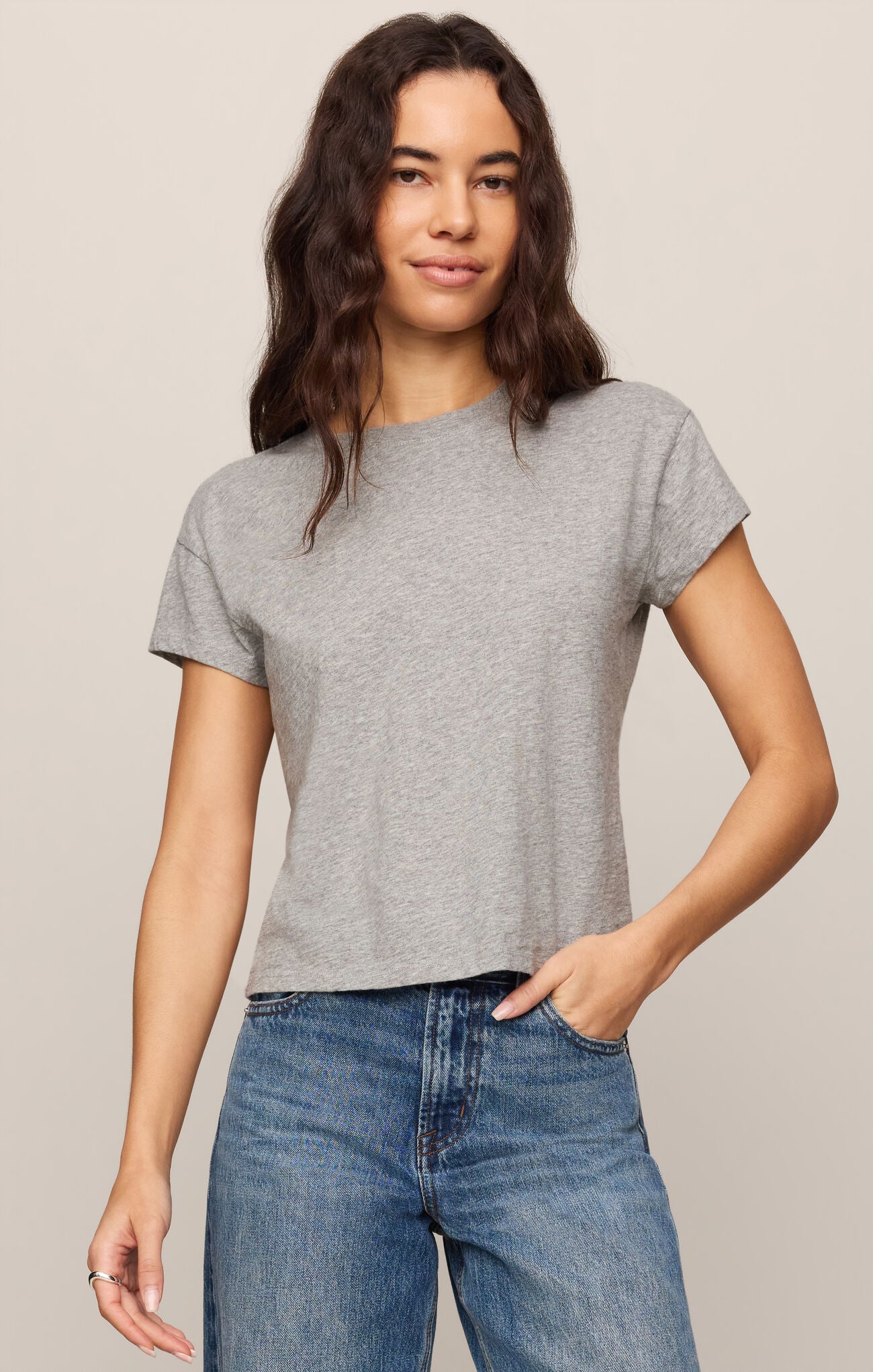Woman wearing a gray t-shirt and blue jeans against a beige background