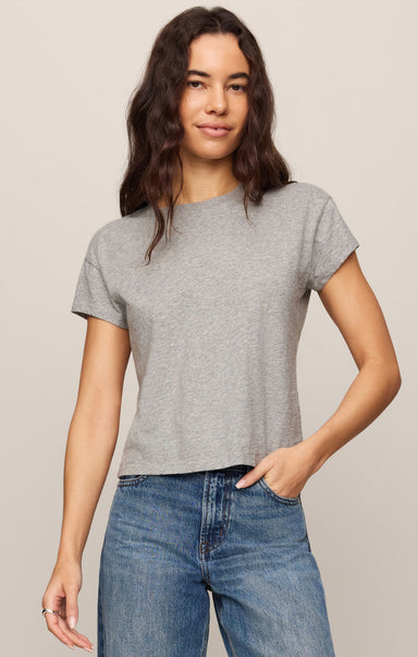 Woman wearing a gray t-shirt and blue jeans against a beige background
