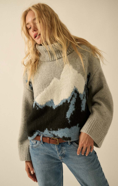 Woman wearing a sweater with mountain design against a plain background