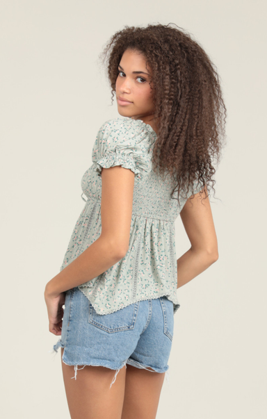 Woman wearing a light green floral blouse and denim shorts on a beige background