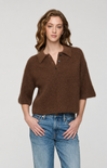 A woman modeling a brown fuzzy knit polo sweater with three-quarter sleeves and a buttoned collar, paired with blue jeans, against a light gray studio background.
