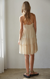 Woman wearing a beige tiered dress standing against a plain wall.
