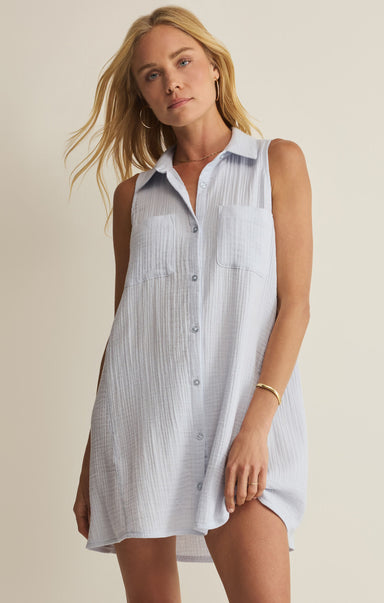 Woman wearing a sleeveless, light-colored shirt dress against a plain background