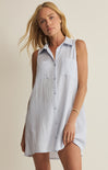 Woman wearing a sleeveless, light-colored shirt dress against a plain background