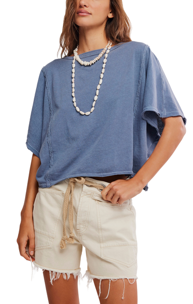 Woman wearing a blue oversized shirt and beige shorts with a white background