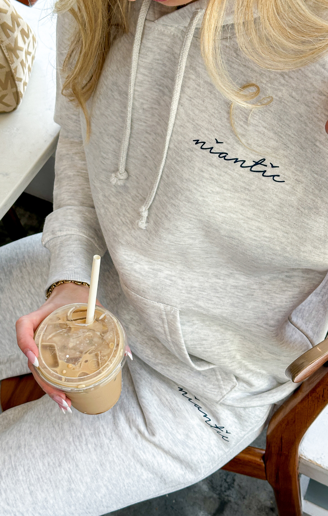 Person wearing a gray hoodie with 'niantic' branding, holding an iced coffee.