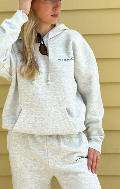 Person wearing a light gray hoodie and pants with 'niantic' branding, standing against a beige wall.