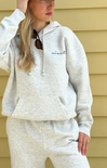 Person wearing a light gray hoodie and pants with 'niantic' branding, standing against a beige wall.
