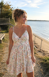 Woman in a floral dress standing by a body of water with a scenic background