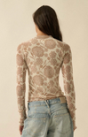 A woman viewed from the back wearing a fitted long-sleeve top with an allover floral pattern in warm beige and brown tones, paired with light blue jeans against a plain cream background.