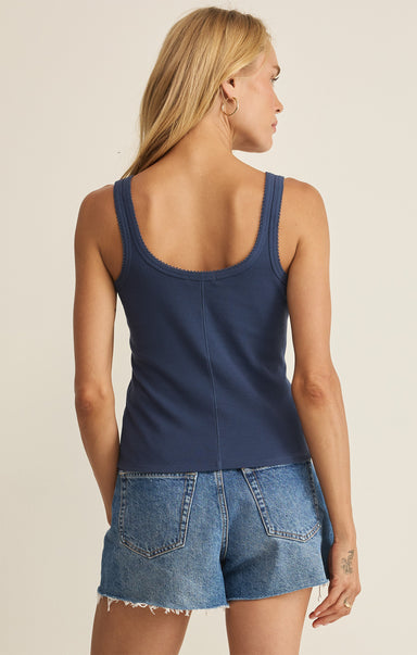 Woman wearing a navy tank top and denim shorts on a beige background
