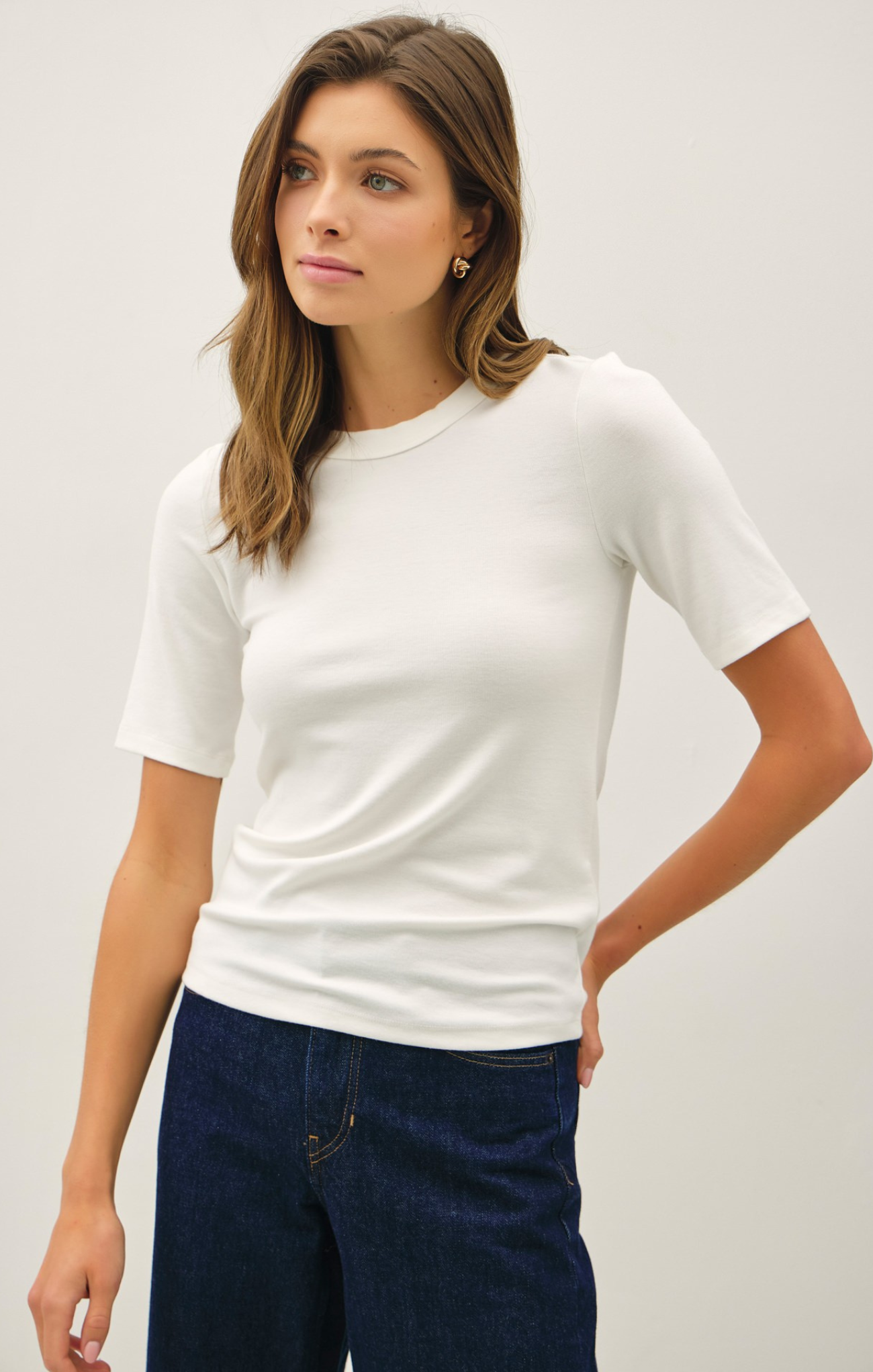 Woman wearing a white t-shirt and blue jeans against a plain background