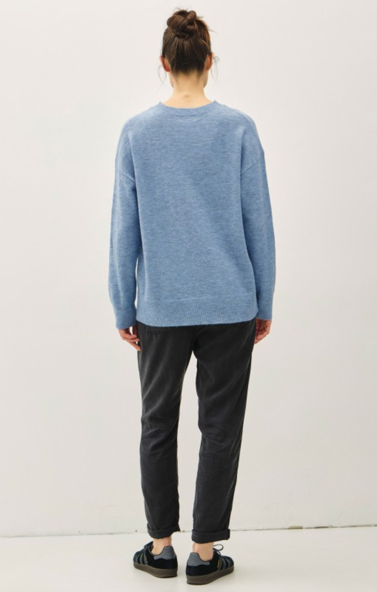 Person wearing a blue sweater and dark pants on a white background