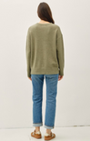 Person wearing a green sweater and blue jeans on a white background