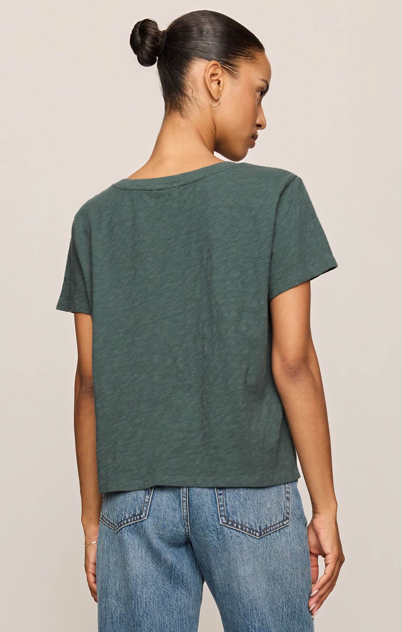 Person wearing a green t-shirt and blue jeans on a beige background