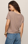 Woman wearing a brown t-shirt and blue jeans against a beige background